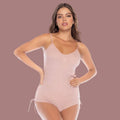 Woman wearing a blush one-piece PJ set with thin shoulder straps and pull strings on the hips.