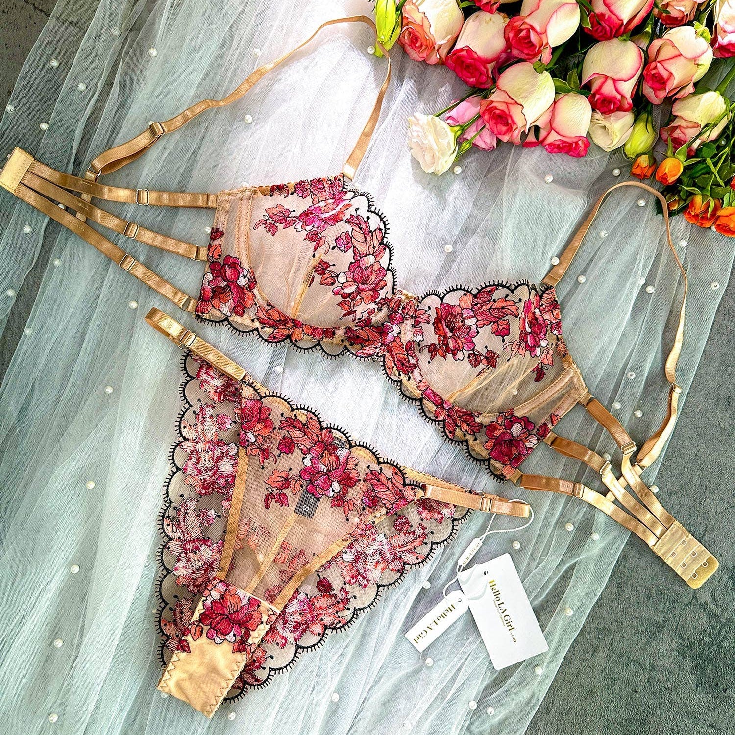 Floral lingerie set with gold accents on a light fabric background, accompanied by flowers.