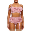 A model wearing a pink lingerie set consisting of a cold-shoulder crop top with a front bow, a matching high-waisted garter belt with front buttons, a matching panty, and sheer thigh-high stockings, paired with clear platform heels against a white background.