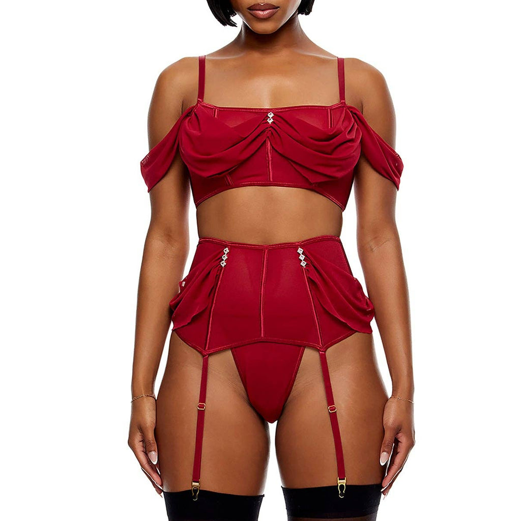 A model wearing a red lingerie set consisting of a cold-shoulder crop top, a high-waisted garter belt with matching thong, and attached garter straps, paired with sheer black thigh-high stockings and black pointed-toe heels, against a plain white background.