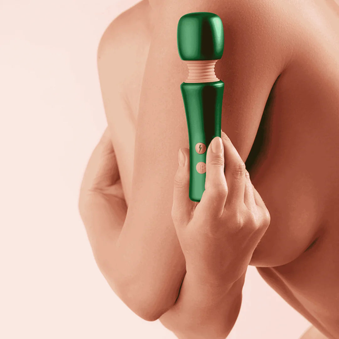 Person using a green handheld massager on their back against a pink background