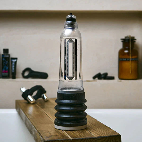 Clear and black cylindrical penis pump on a wooden block over a bathtub.