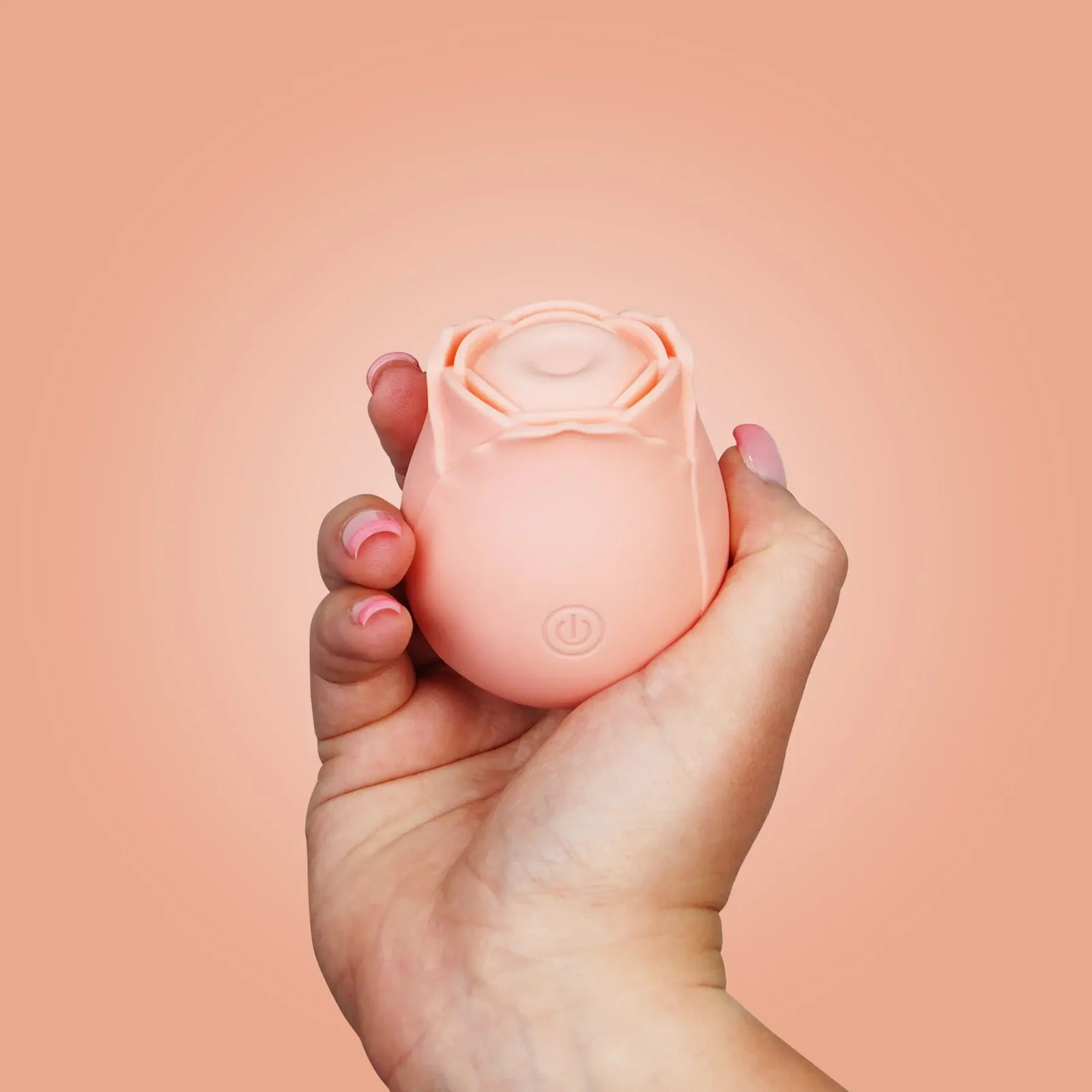 Hand holding a pink rose-shaped device against a peach background