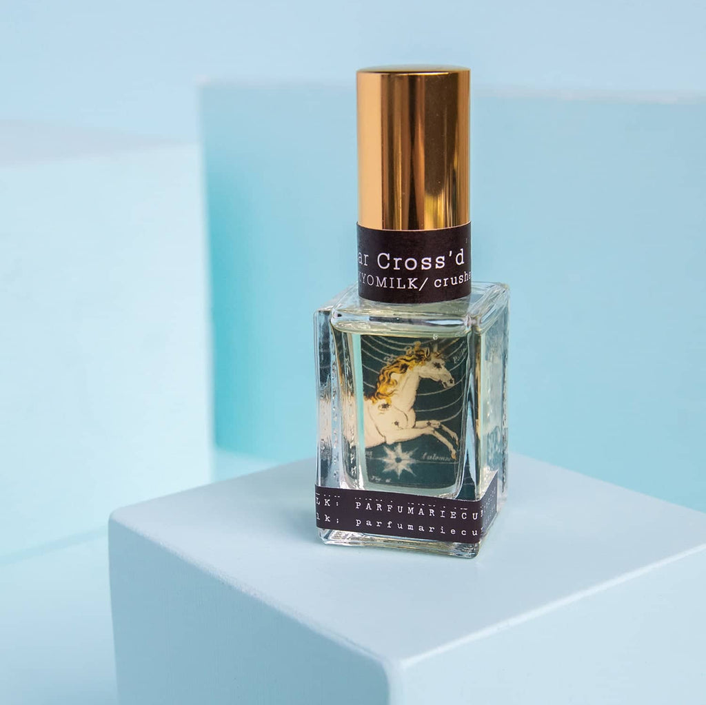 Perfume bottle with gold cap and unicorn label on a light blue background