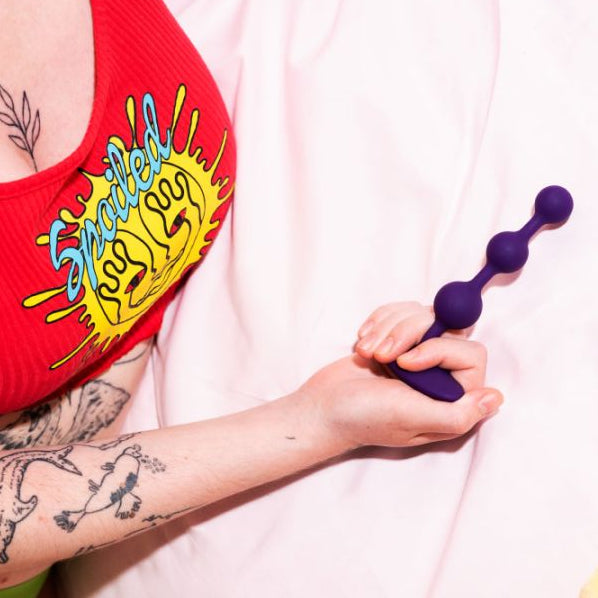 Person wearing a red tank top with a colorful graphic design, holding a purple object on a white background.