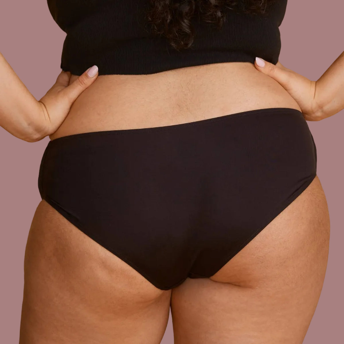 A model from behind wearing a black panties, showing the back of the panties offer full coverage.
