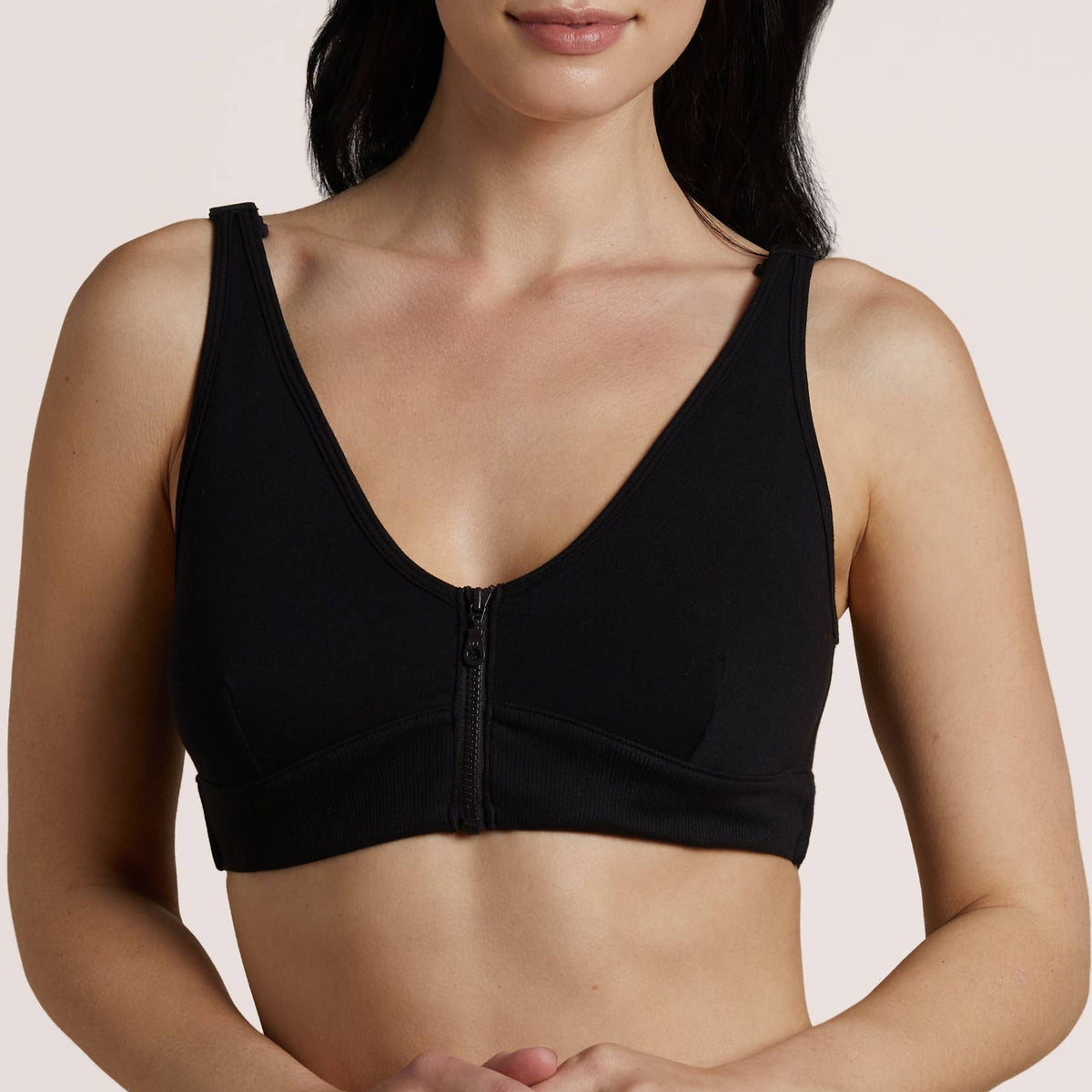 A woman modeling a black wireless bralette with a center zipper, photographed against a solid light beige studio background.