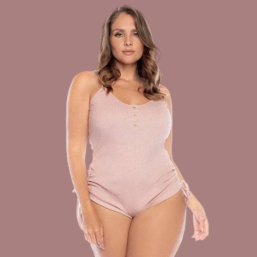 Woman wearing a blush one-piece PJ set with thin shoulder straps and pull strings on the hips.