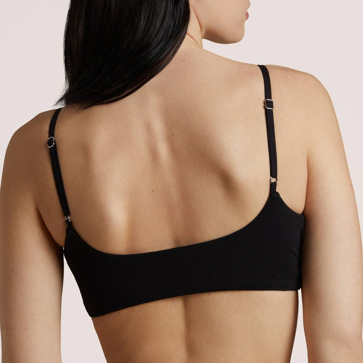 A woman with long black hair is shown from the back wearing a black bralette.