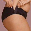 A woman modeling a black panties, showing how the hips have hook and eye closures that make it possible to put them on if you have limited mobility.