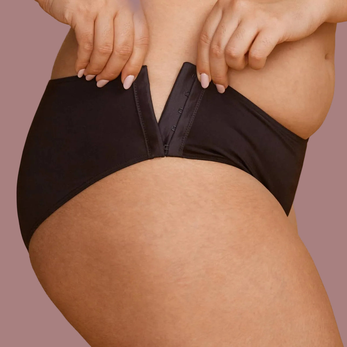 A woman modeling a black panties, showing how the hips have hook and eye closures that make it possible to put them on if you have limited mobility.