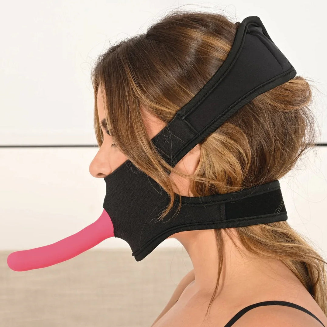 Side view of the gag, with a dildo facing out of the mouth hole and two secure straps holing it in pace behind the neck and at the top of her head.