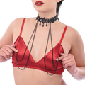 A woman modeling a red satin lingerie set with a matching red thong and red bra, accessorized with a black beaded choker and double chain drapes against a plain white background.