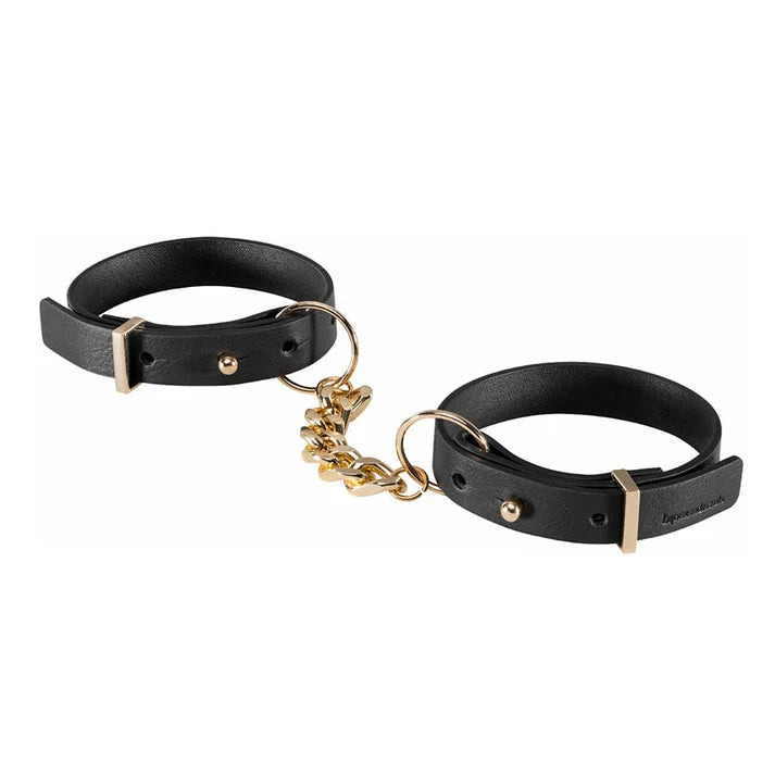 Two thin faux leather cuffs with hole and button closures and a gold hue connector chain.