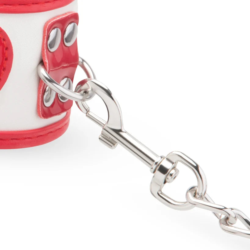 Close-up of a white and red padded cuff with silver metal rings, studs, and a silver swivel clasp attached to a chain, on a white background.