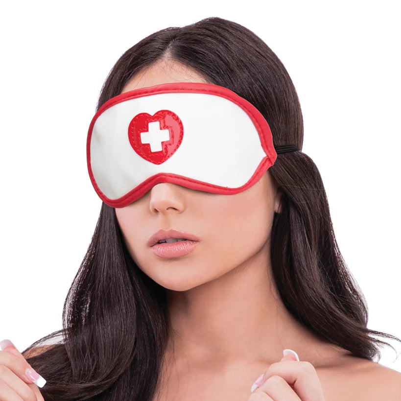 A woman wearing a white blindfold with a red border and a red heart with a white cross on the front, shown against a plain white background.
