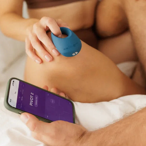 A couple, with legs entangles, holding the Pivot and a phone with the app open.