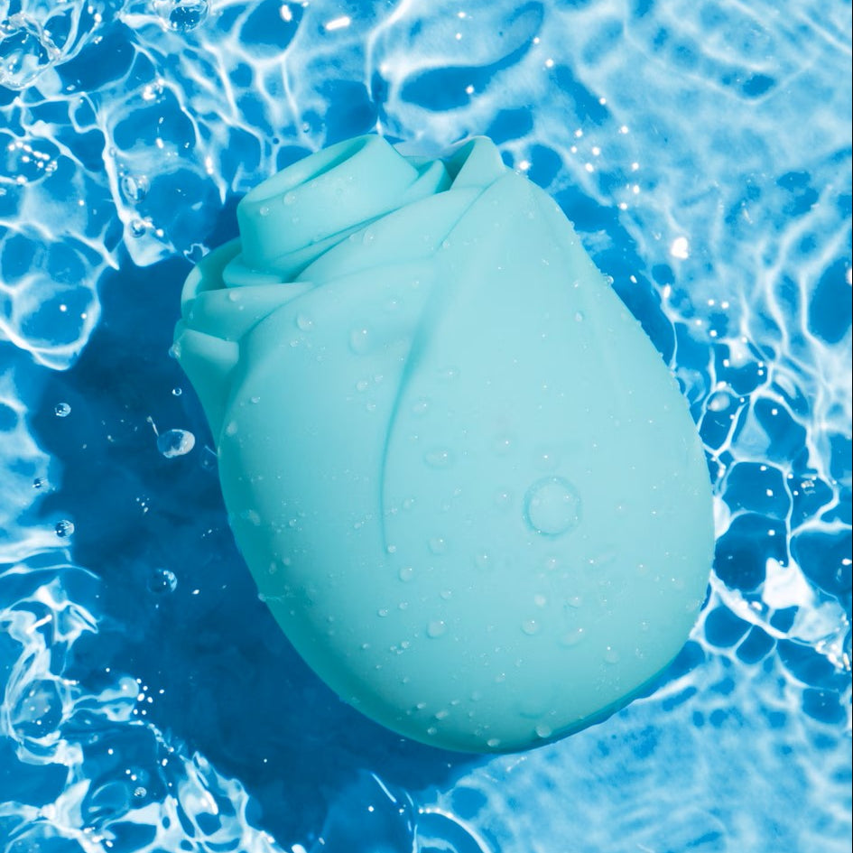 A light blue silicone rose-shaped toy resting on rippling blue water with water droplets on its surface.
