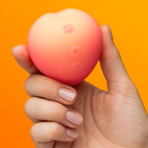 Hand holding a peach-shaped sex toy against an orange background