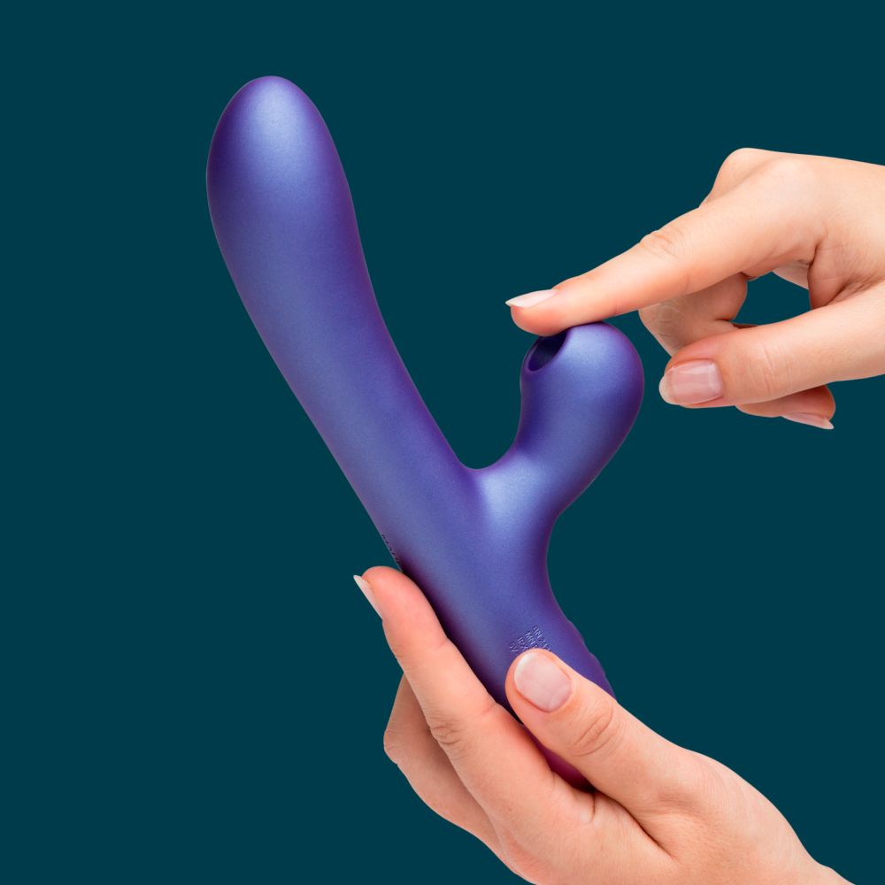 A person holds a matte purple curved personal massager with a small side button, shown against a solid dark teal background.