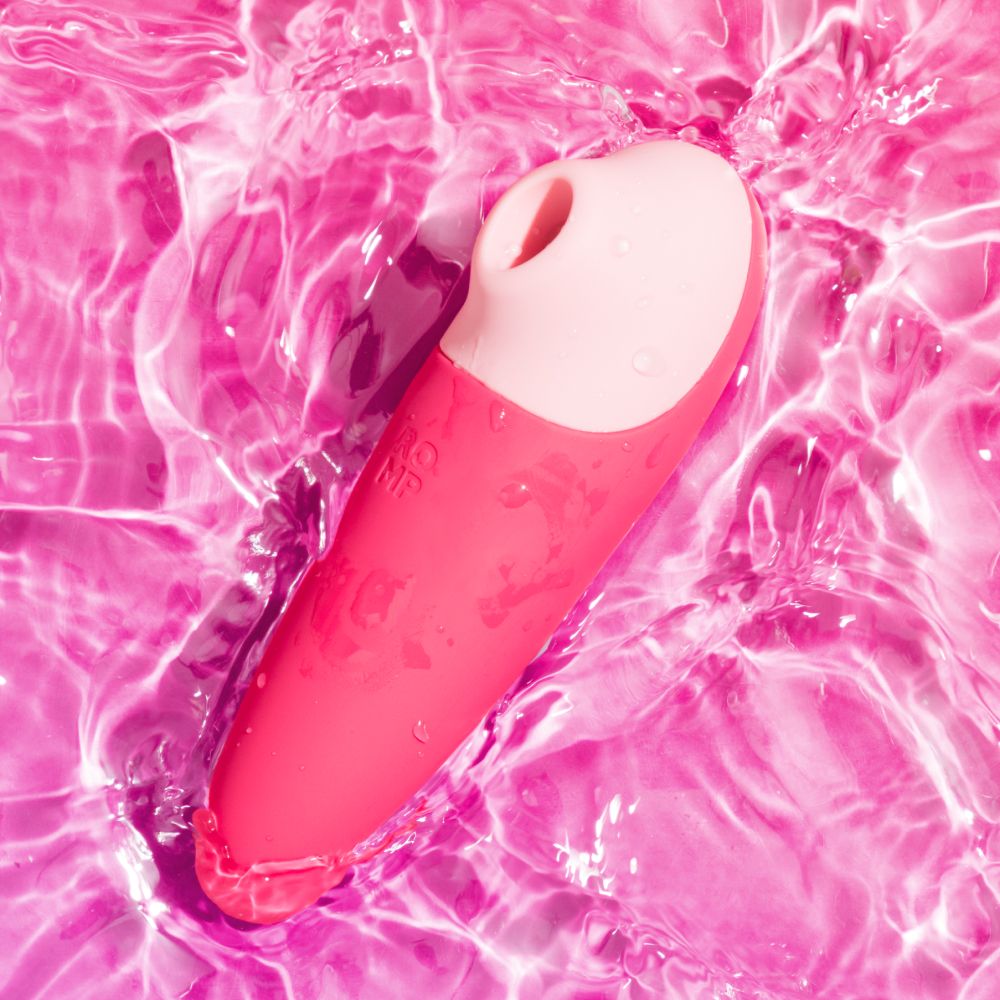 A pink personal massager with a white curved tip, shown floating on rippling pink water.