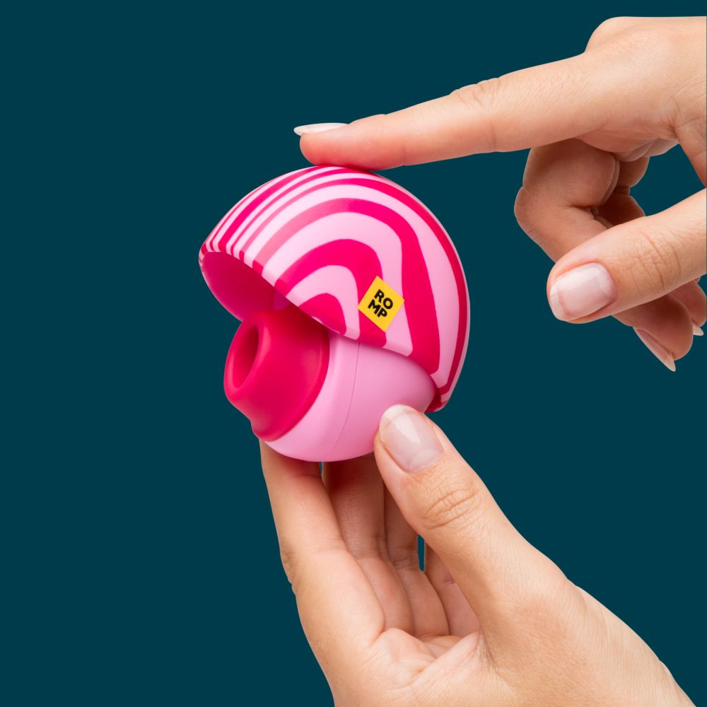 A hand holds a small half-circle-shaped pink and white striped novelty item while another hand points at it, against a dark teal background.