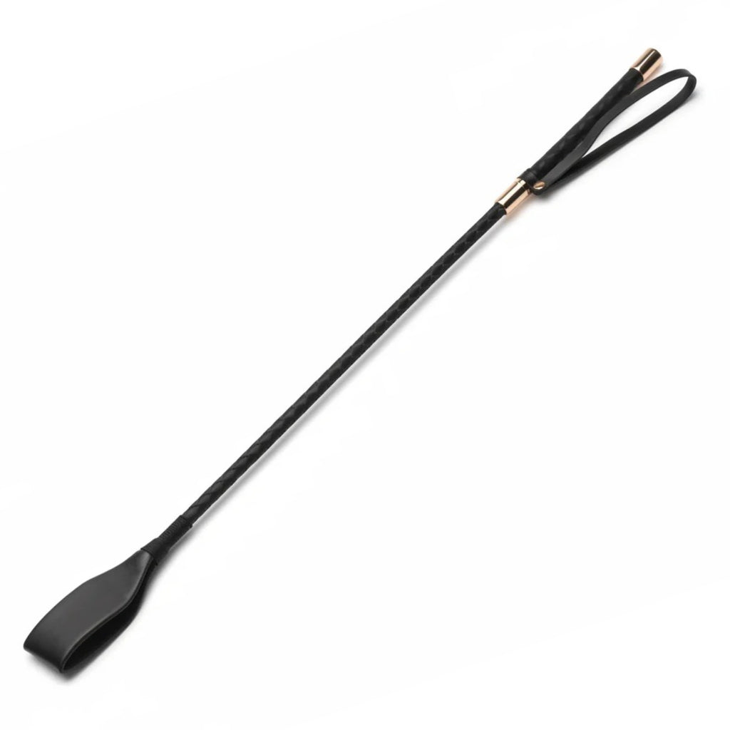 A black riding crop with a textured handle, a black leather loop, and small gold-toned metal accents, shown diagonally on a plain white background.